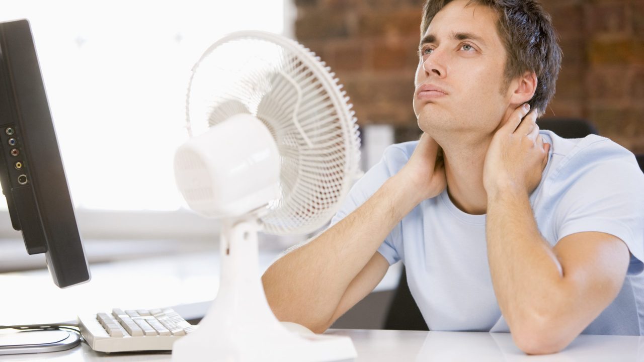 Businessman in office with computer and fan cooling off